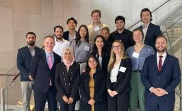 A group of students and faculty standing with an alumnus on a staircase.