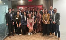 A group of students and alumni standing in front of the logo of the University of Chicago.