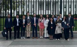 A group of students stand in front of a large black fence with the north face of the US White House in the background.